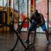 A muscular man intensely exercises with battle ropes in an indoor gym setting, showcasing strength and fitness.