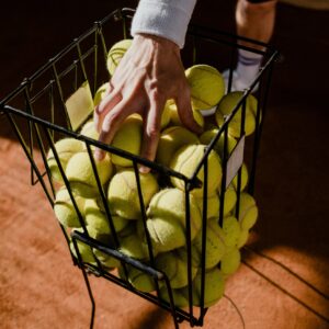 A tennis player collecting balls from a basket on a clay court, highlighting a close-up shot and sportive theme.